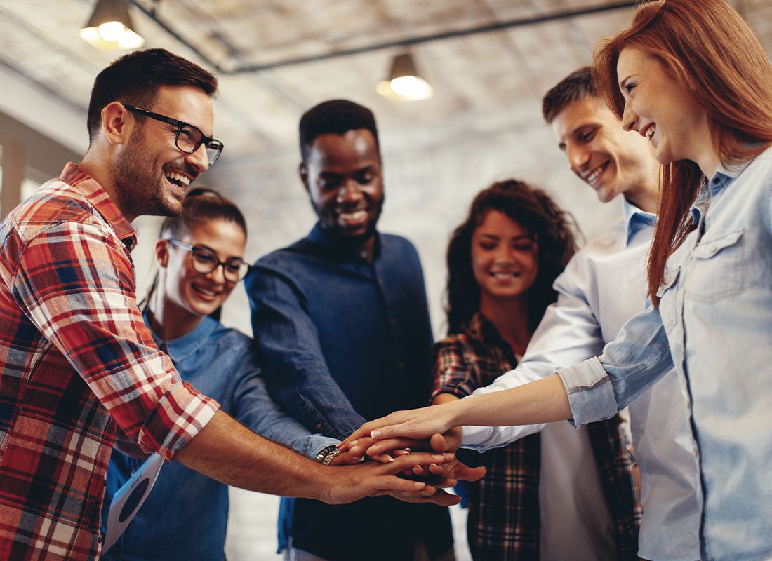 Business Insurance - Teamwork in the Office With Smiling Employees Placing Hands on One Another in a Circle