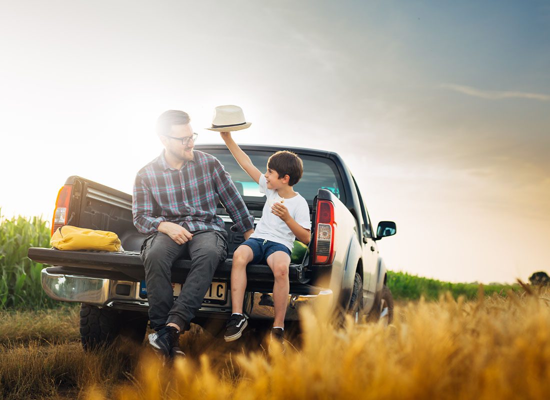 Insurance Solutions - Father and Son Having Fun in the Back of a Pickup Truck in a Field at Dusk