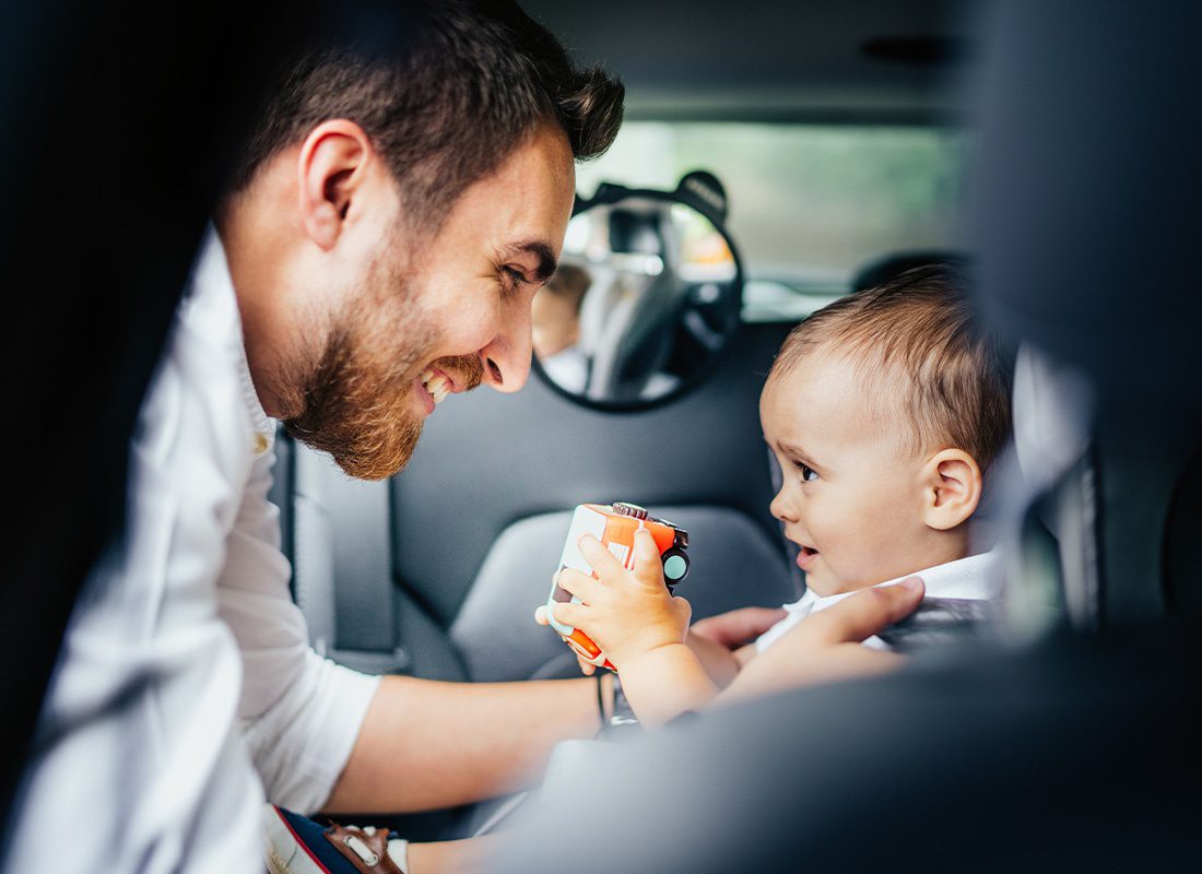 Personal Insurance - Smiling Father Placing Infant Son in a Car Seat Closeup